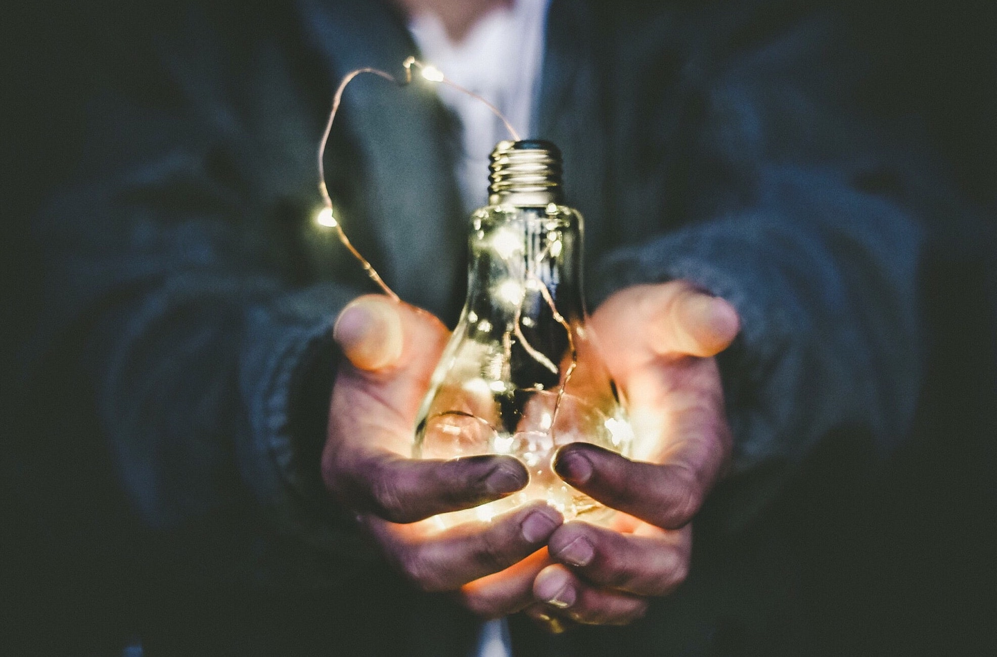 Cupped hands holding a lit lightbulb